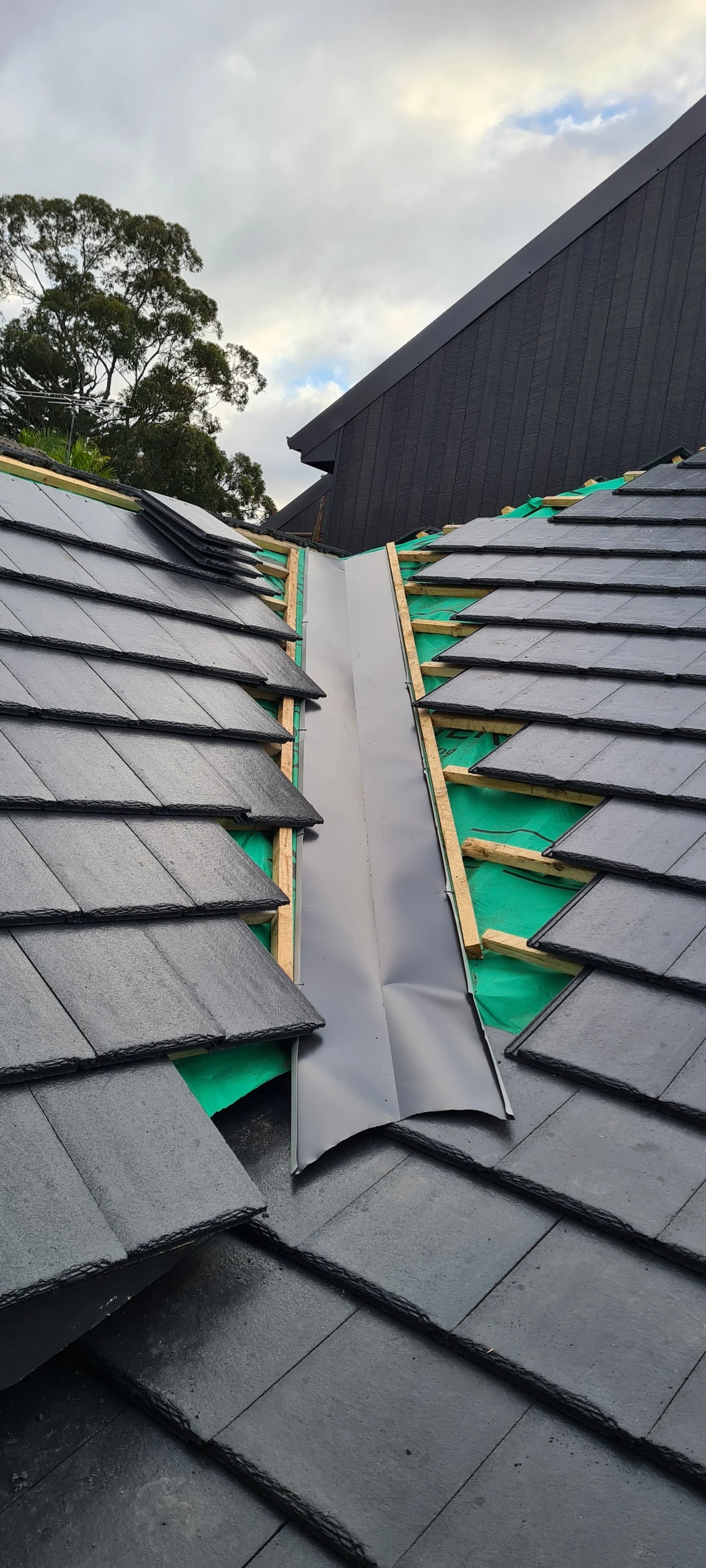 Roof under construction with dark gray shingles and missing middle section covered with water-resistant flashing