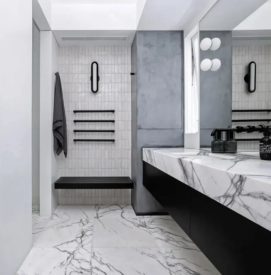 Modern bathroom with marble floor and countertop, gray and black accents, towel, and black wall-mounted lighting.