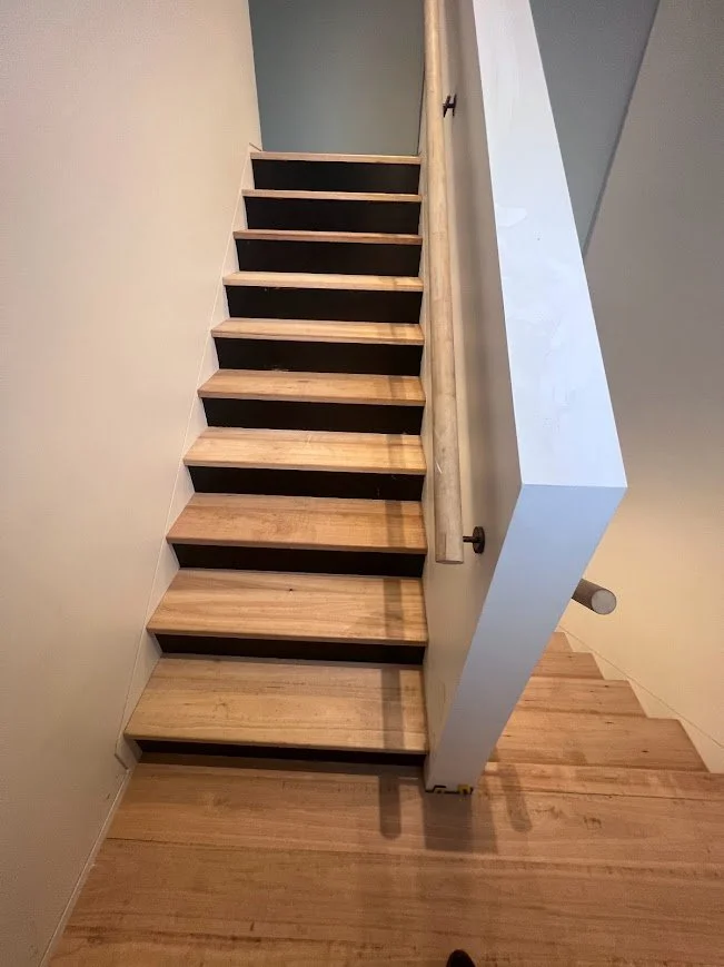 Wooden staircase with black treads and a white wall and railing.