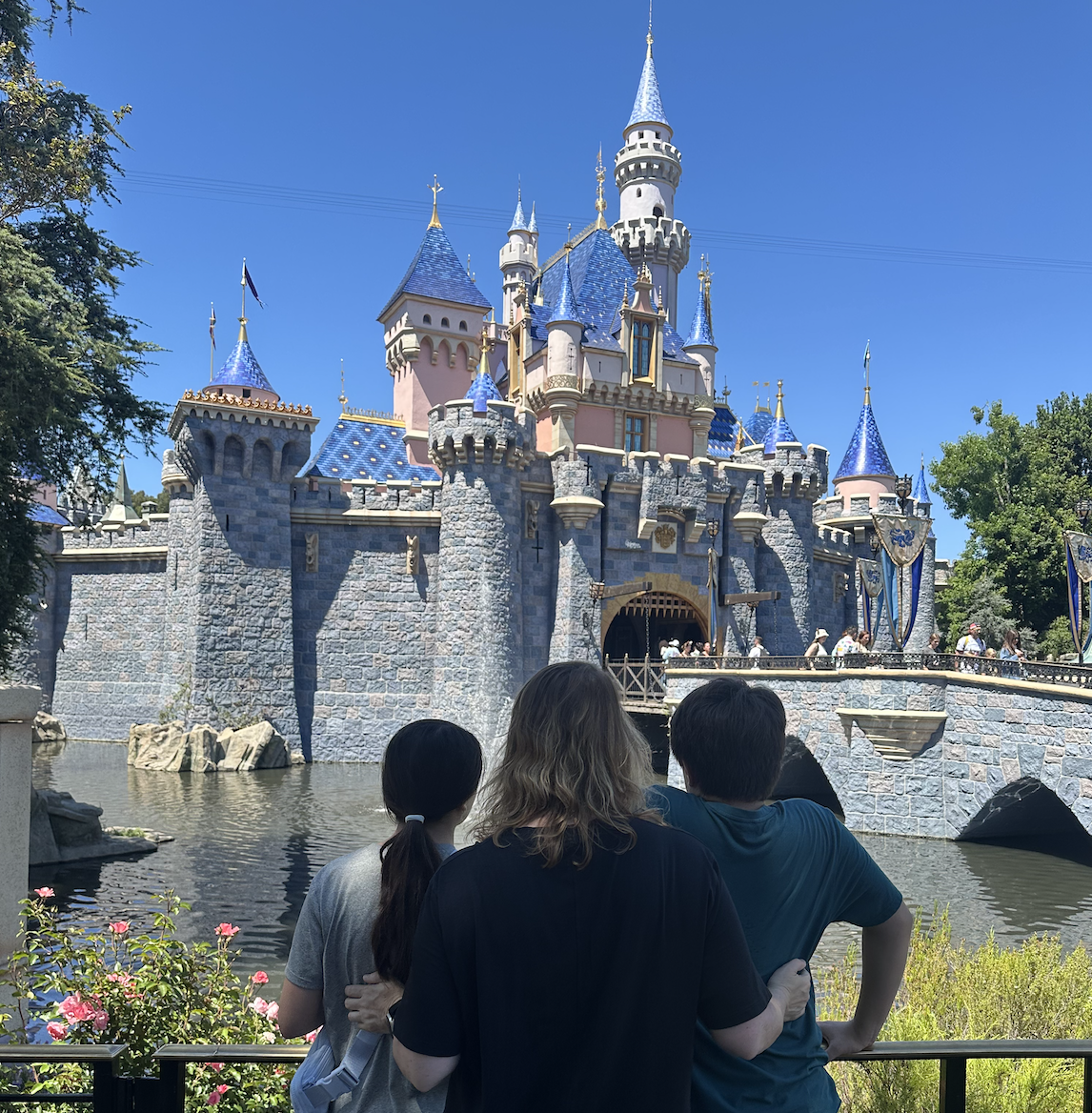 woman-standing-with-two-kids-in-front-of-sleeping-beautys-castle-at-disneyland