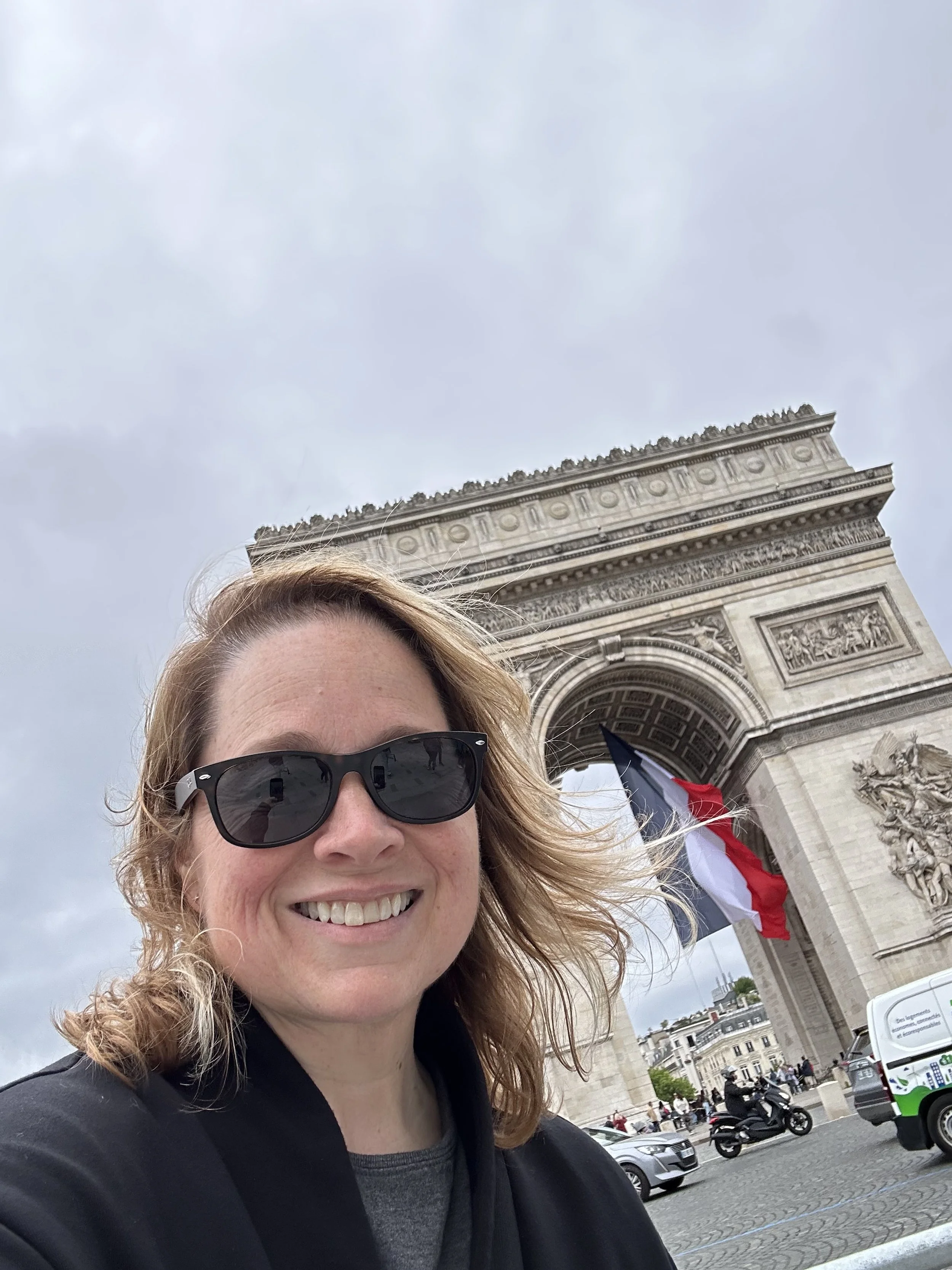 gen-x-woman-with-blonde-and-brown-hair-with-fair-skin-wearing-sunglasses-in-front-of-the-arc-de-triomphe-in-paris
