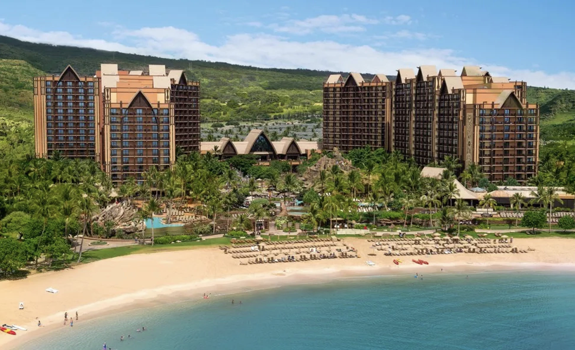 Beachfront resort with tall buildings, swimming pools, palm trees, and sandy beach.