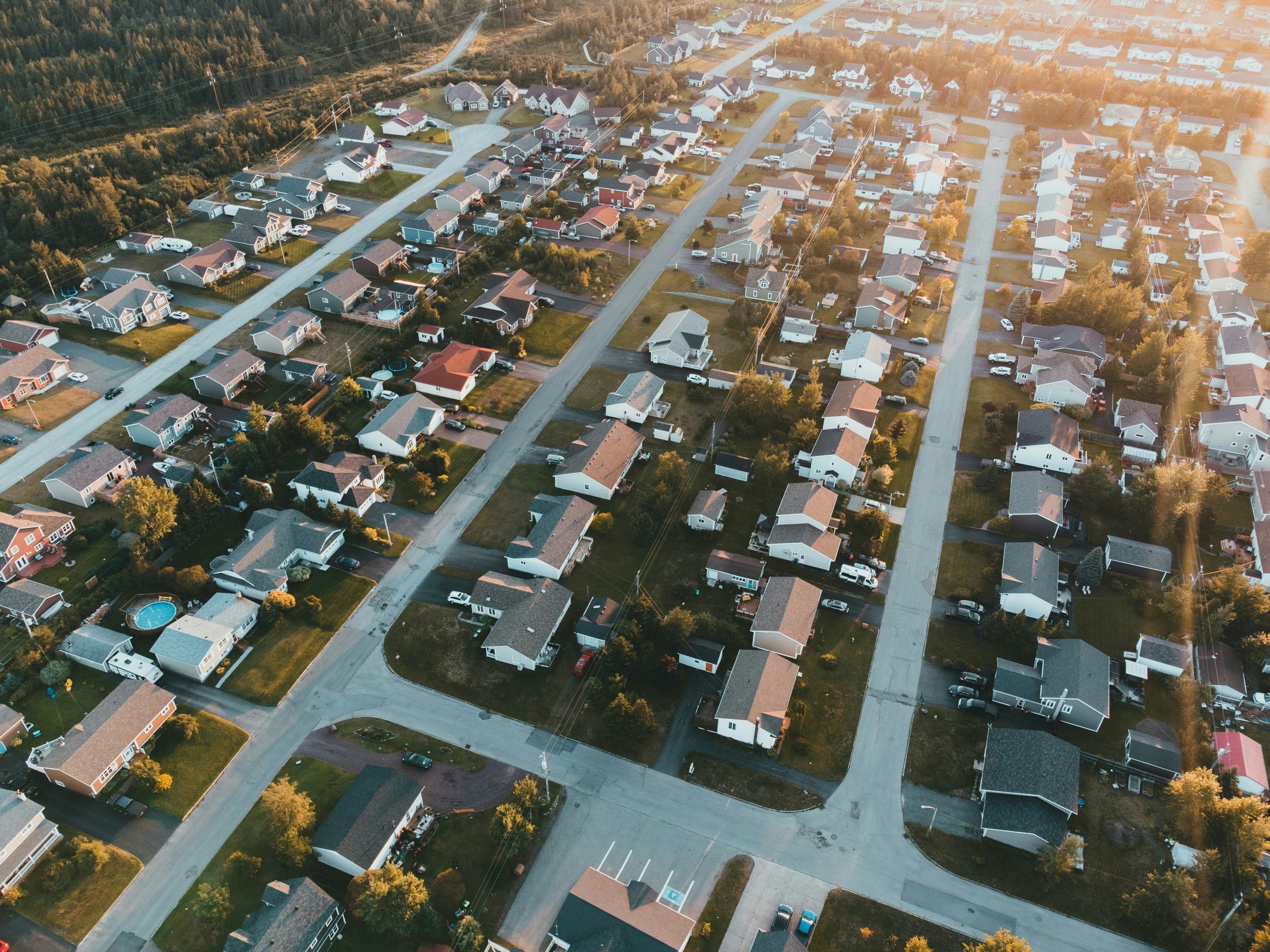 Aerial view of a residential neighborhood with houses, roads, and trees during sunset.