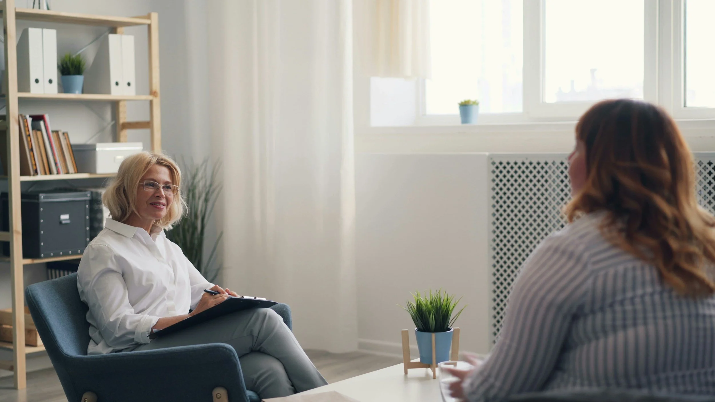 Two women having a conversation in an office, one taking notes and the other listening.