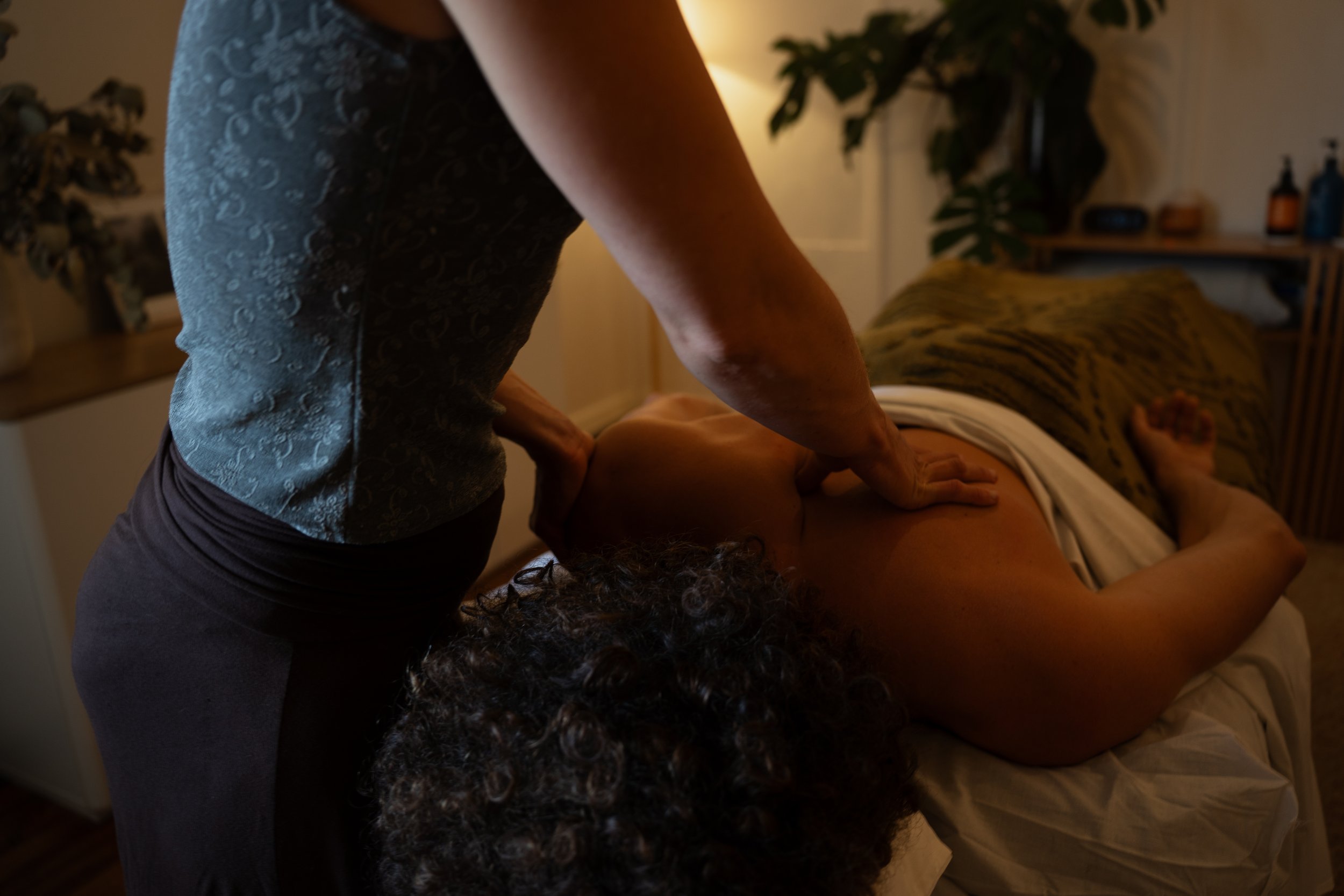 A person giving a massage to another person lying face down on a bed in a dimly lit room.