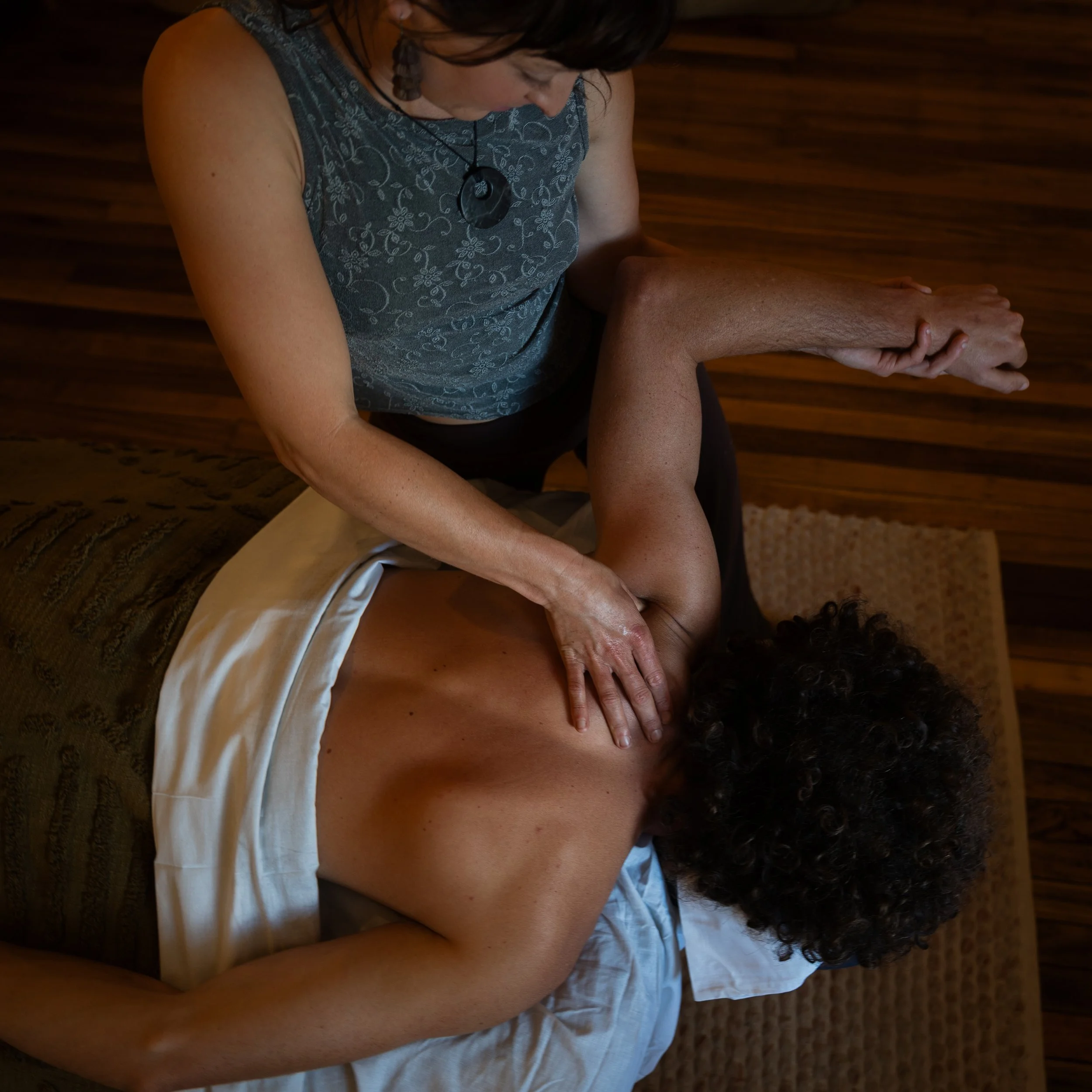 A woman with curly hair lying face down on a massage table, receiving a massage from another person who's hands are on her back.