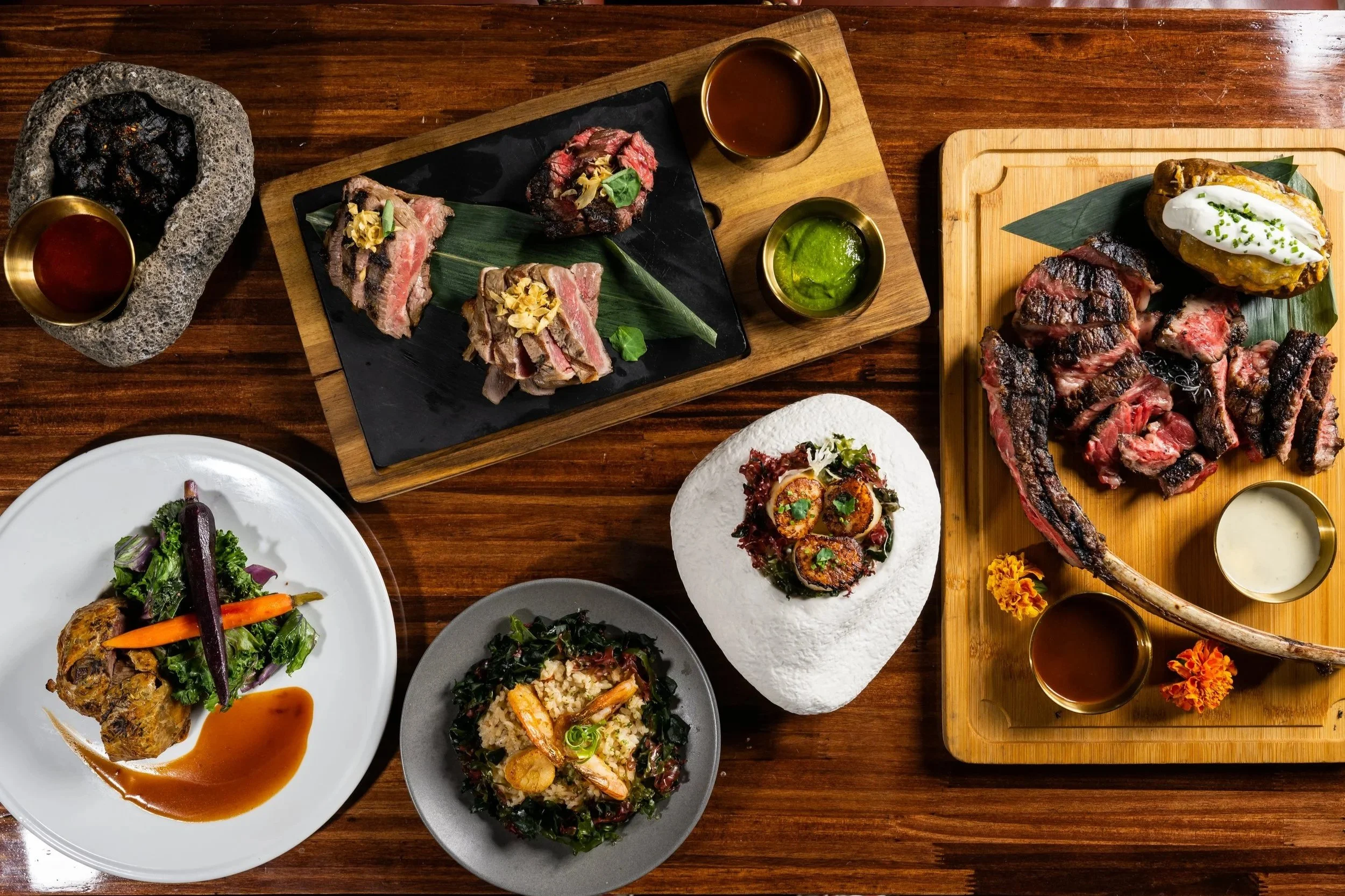 A variety of grilled meats, sauces, and side dishes served on wooden and ceramic plates on a wooden table.