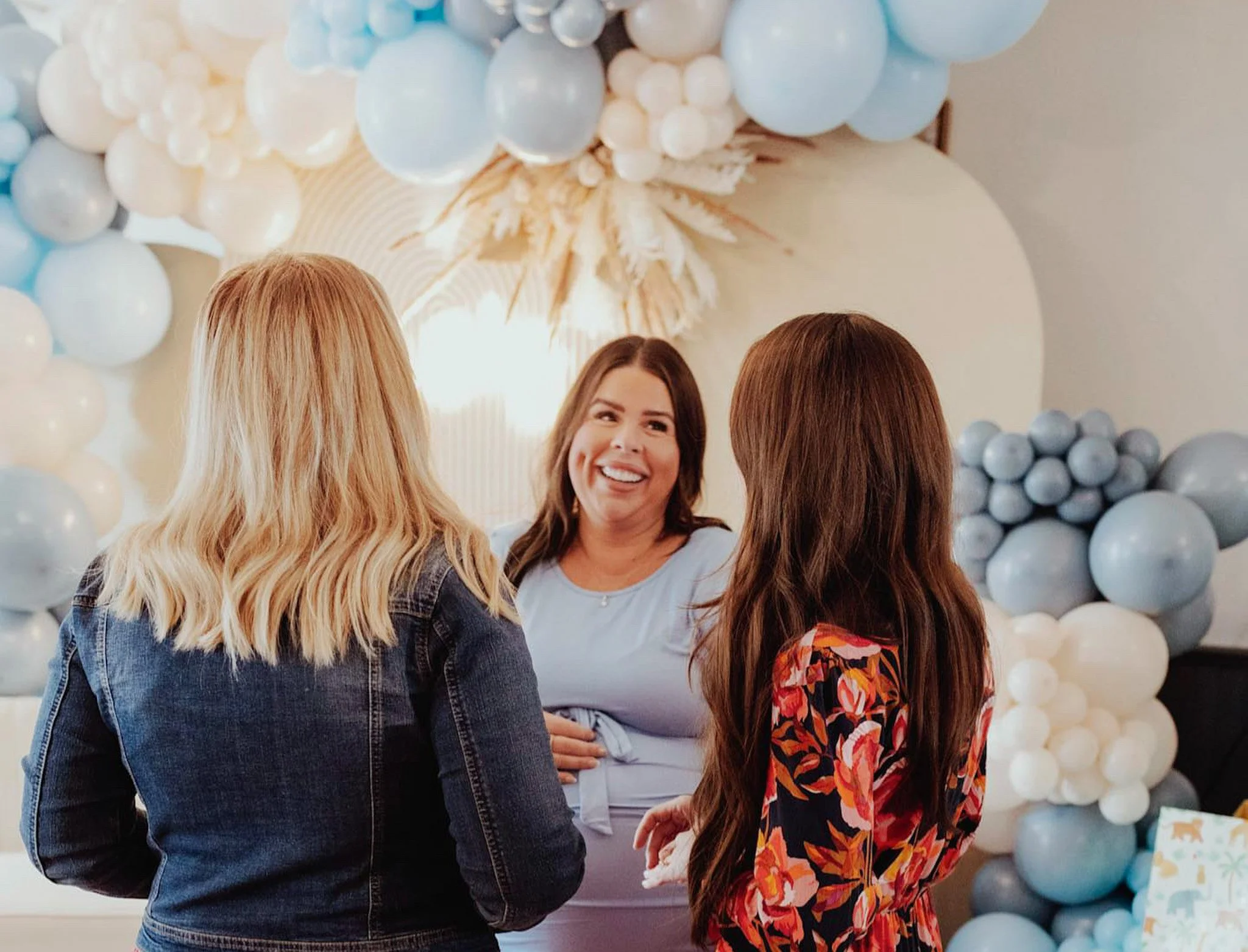 A group of women having conversation at a celebration with balloon decorations in the background.