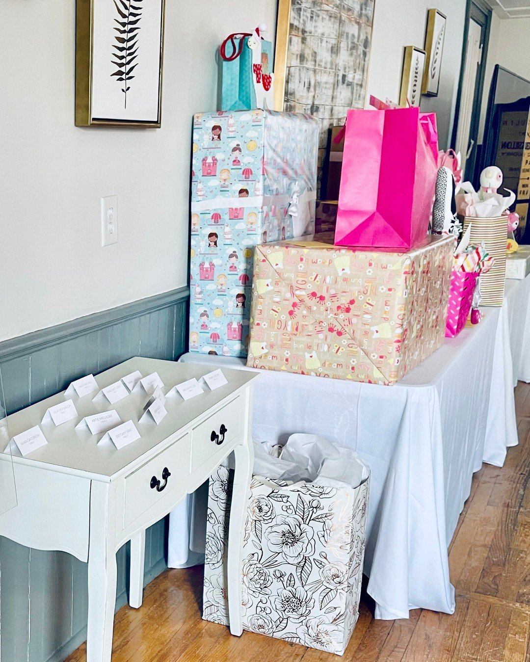 Table with neatly wrapped gift boxes of various sizes, decorated with different themes and colors, set against a wall with framed artwork.