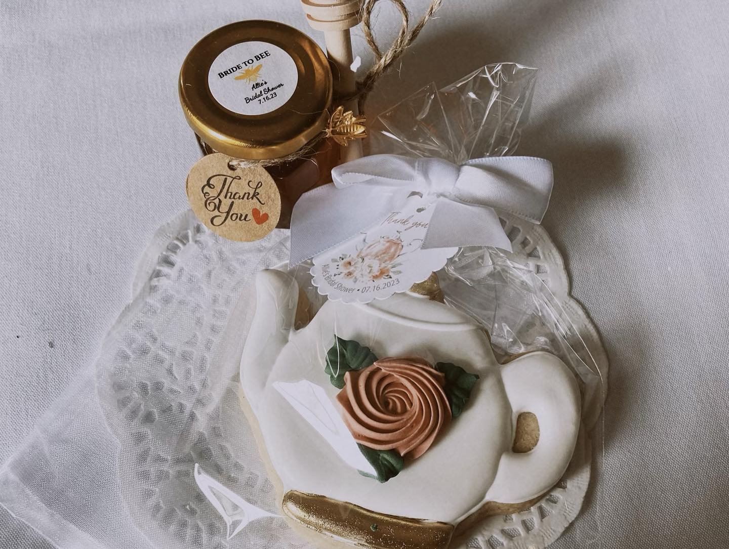 A cupcake with a swirl of pink and green frosting, decorated with a gold heart and a small gold spoon, wrapped in clear plastic.