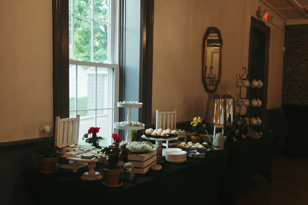 Buffet table with cookies, tea urns, flowers, and cups in a room with a window and vintage decor.
