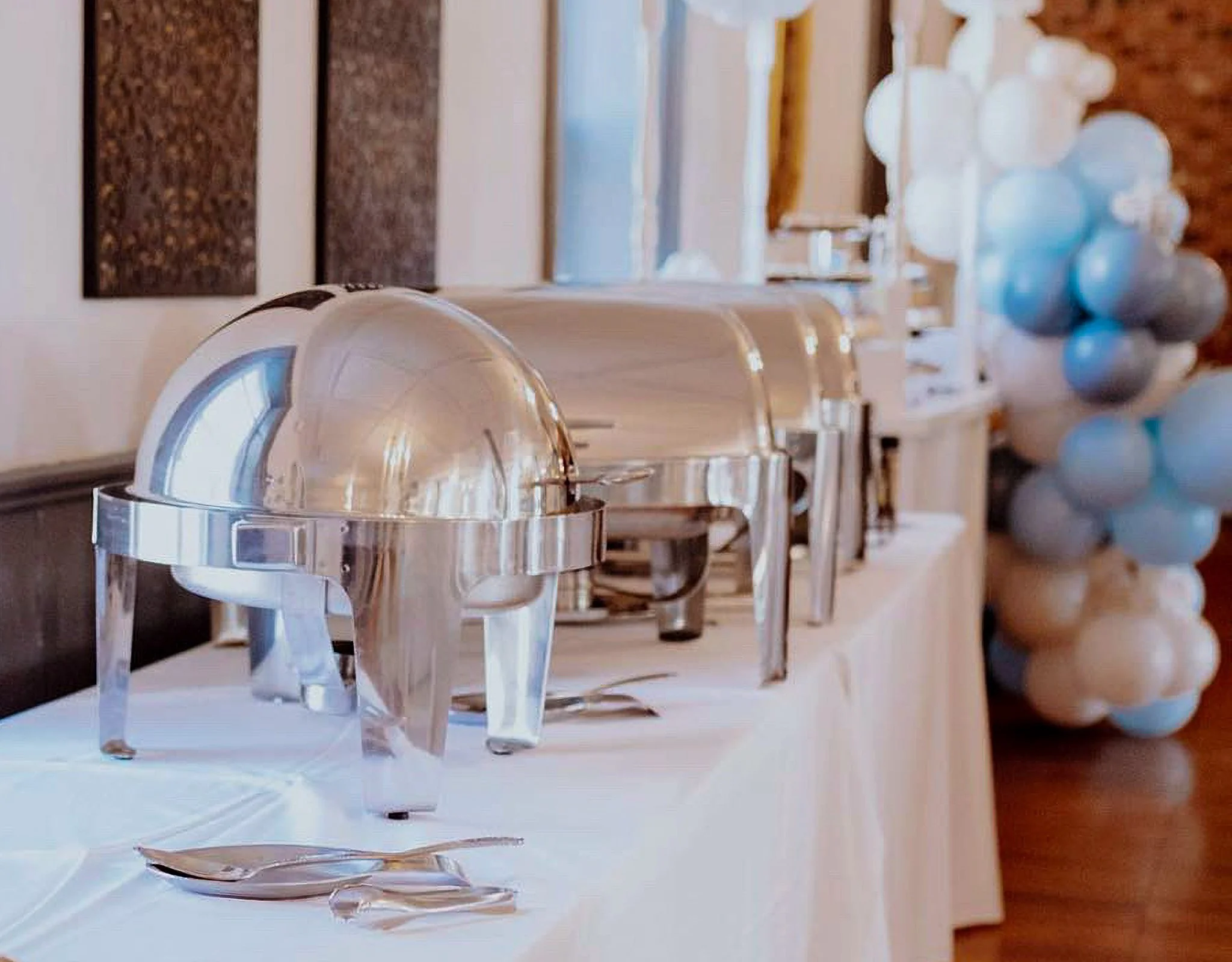 A buffet table with chafing dishes, a bowl of silver balls, and a backsplash of textured brown tiles.