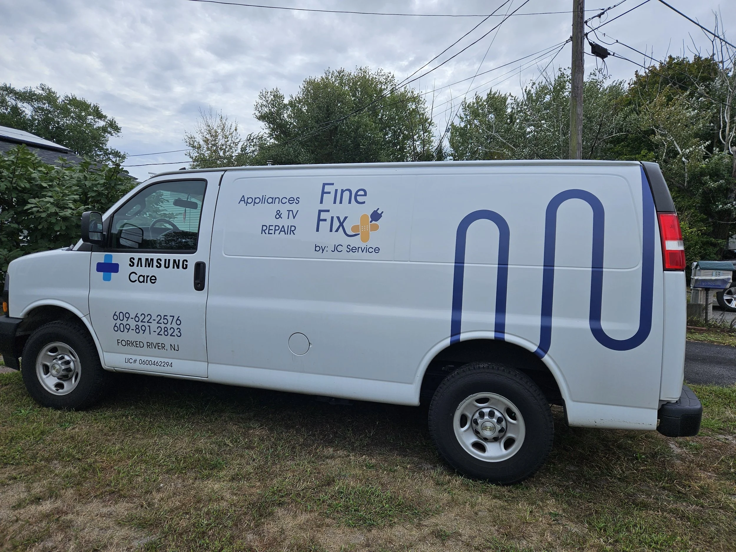 A white delivery van parked on grass with a blue sky and trees in the background. The van has business signage for appliance repair, including a phone number and location in Forked River, NJ, with a Samsung Care logo. Fine Fix by JC service.
We are a