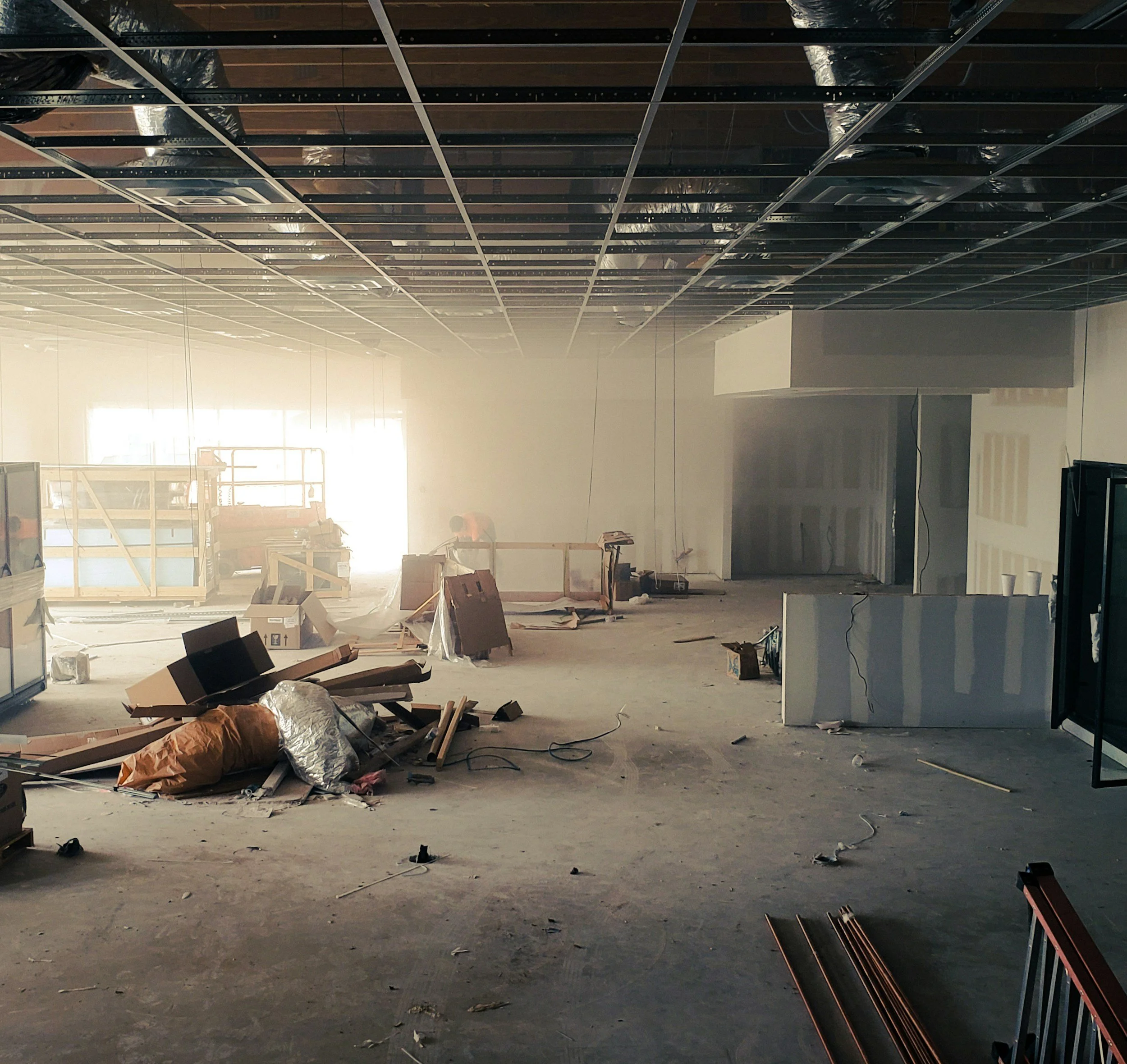Construction site with unfinished ceiling, scattered building materials, and equipment inside a partially developed interior space.