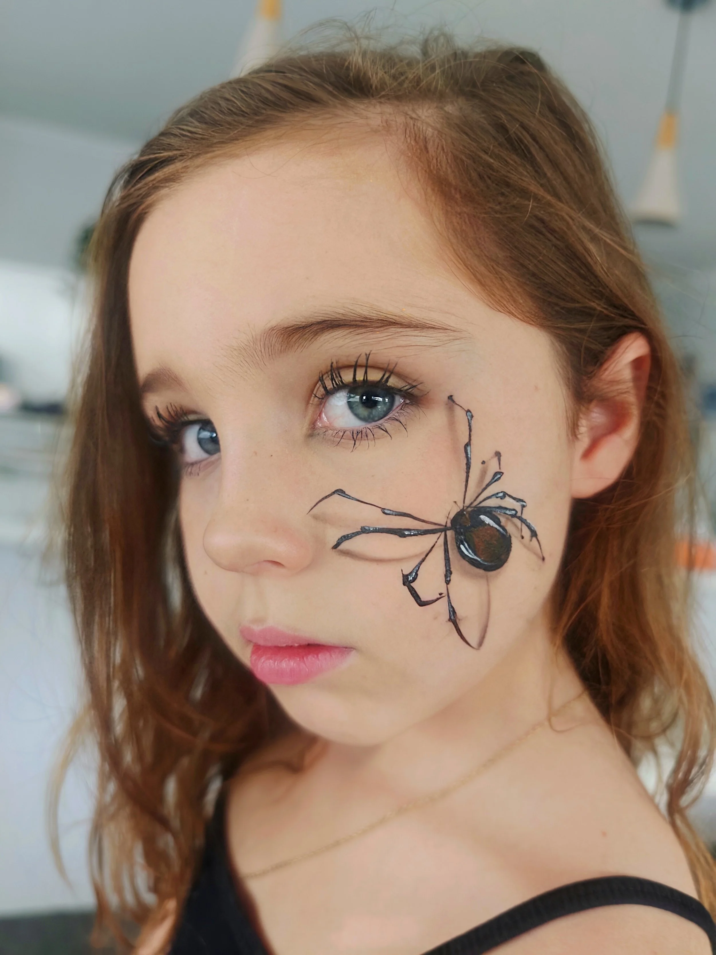 Close-up of a woman's face with blue eyes, red hair, and a painted black spider on her cheek.