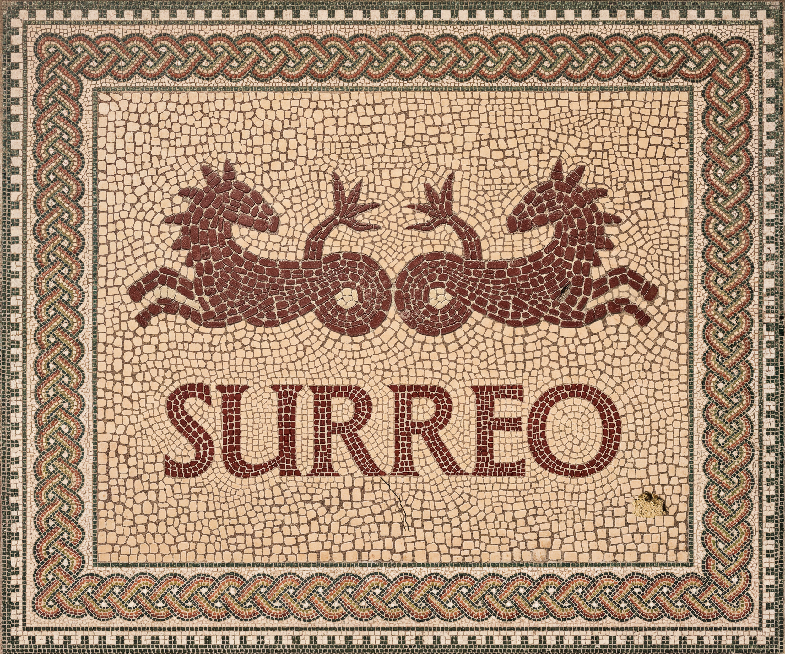 Close-up view of an ancient mosaic floor with a decorative border and a central design featuring two red dragons facing each other. The mosaic is made of small, colored tiles and has a Greek textile pattern border.
