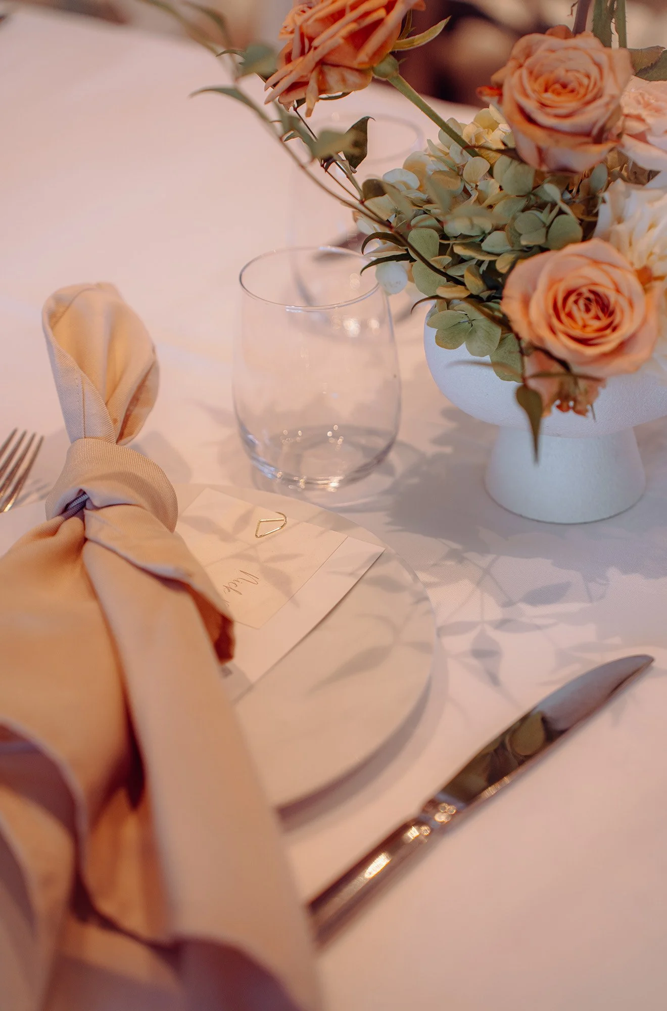 A table setting with a floral centerpiece, a wine glass, a folded cloth napkin, and a dinner knife and fork, all arranged for a formal event.