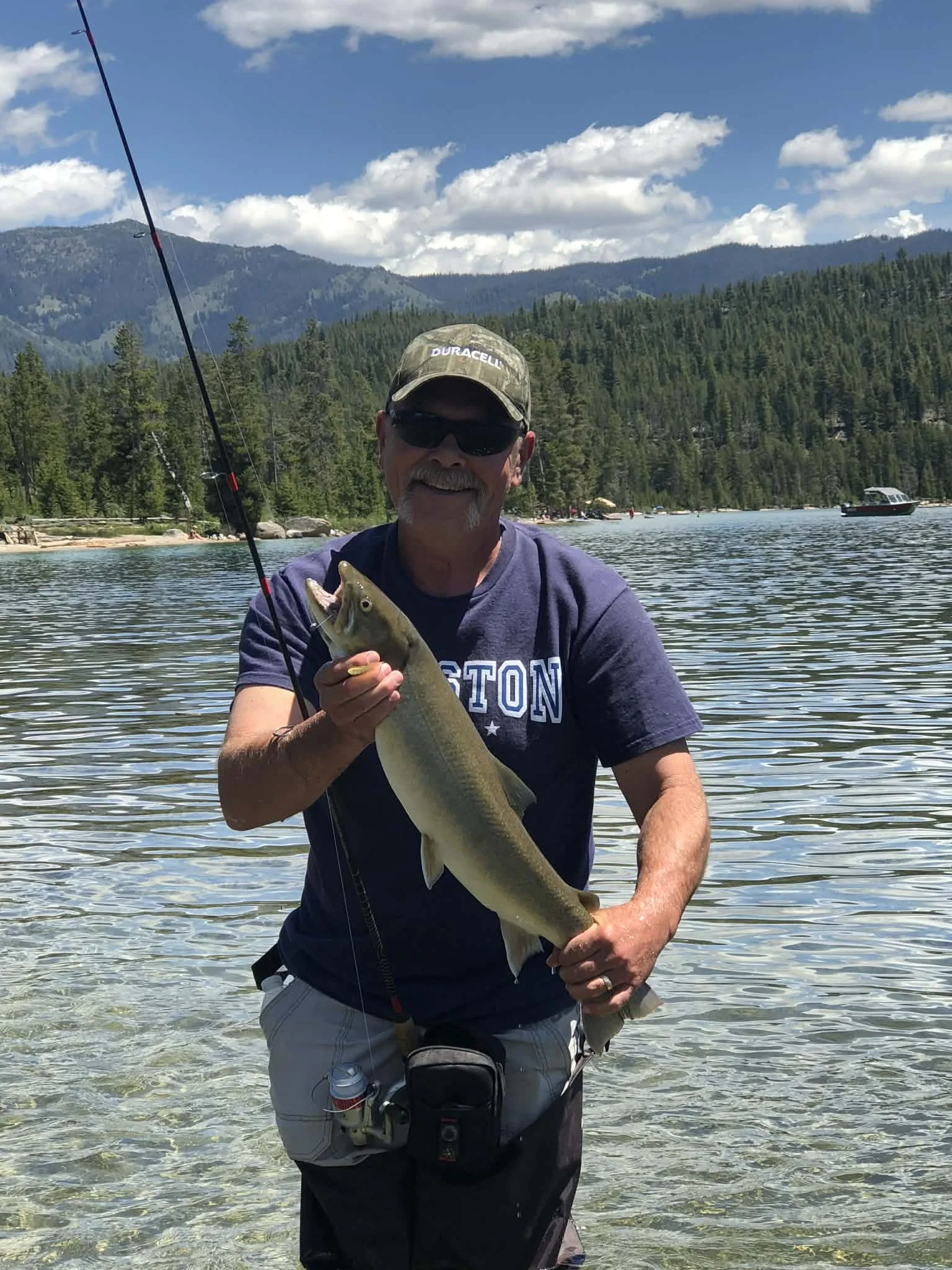 Angler holding a fish beside an Idaho mountain lake representing custom fishing culture and outdoor adventure.