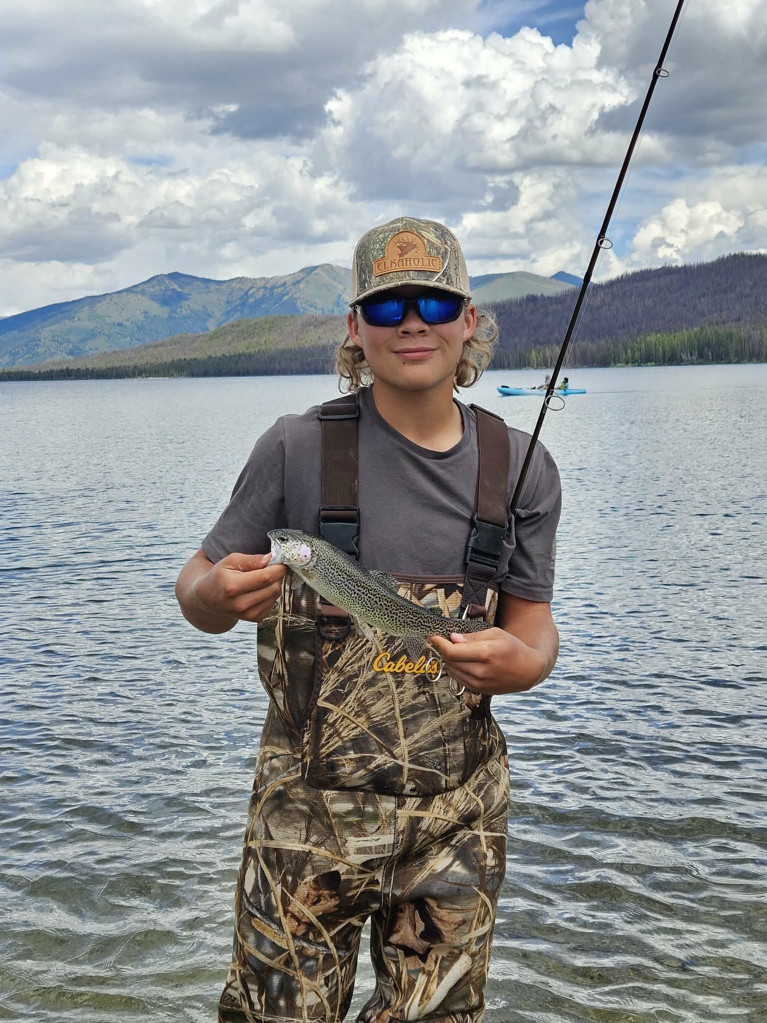 Angler holding a fish beside a mountain lake in Idaho representing the outdoors lifestyle behind Dilly Dahle Custom Rods.