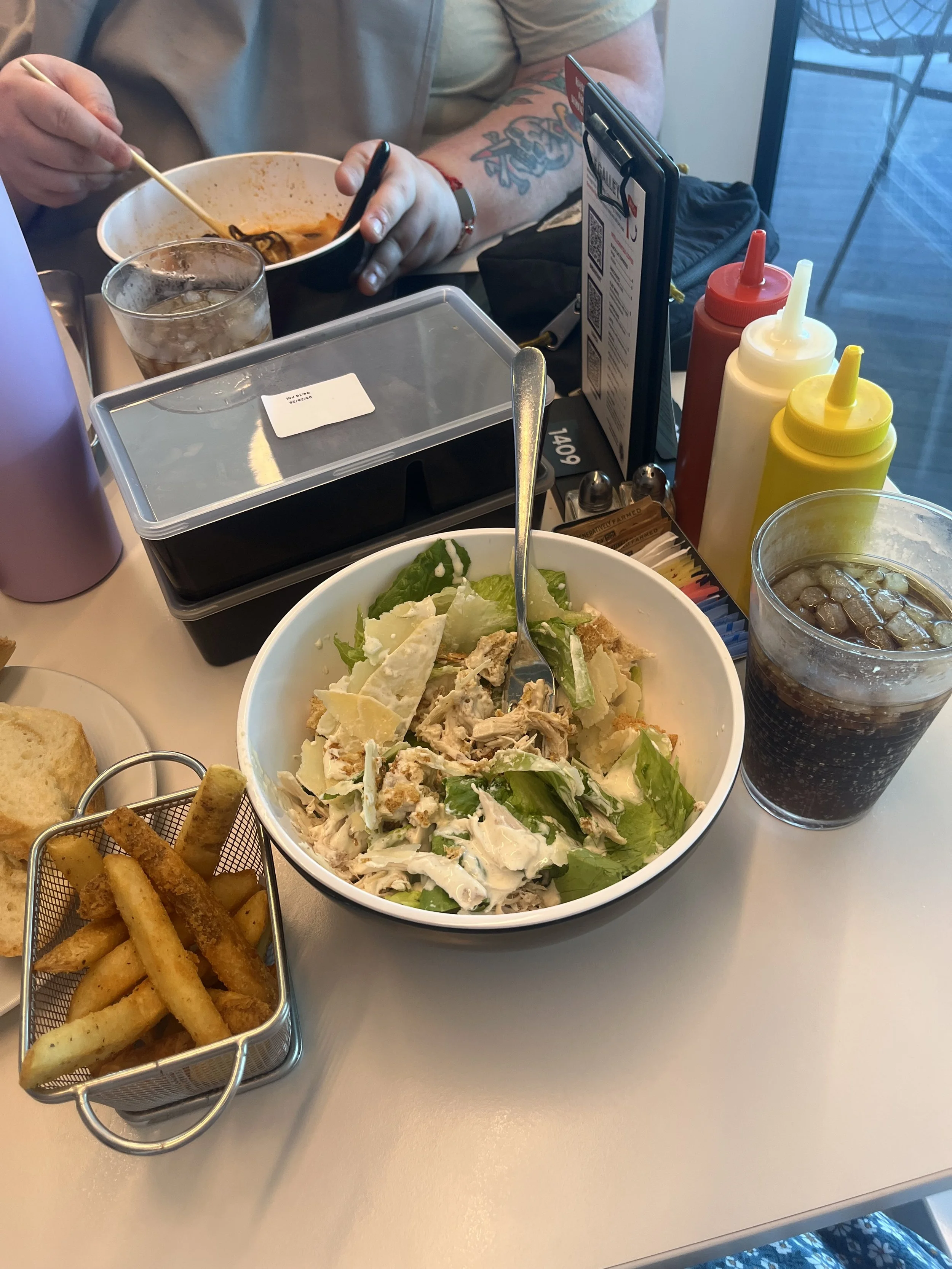 Photo of a caesar salad, french fries, and diet coke on a white table.