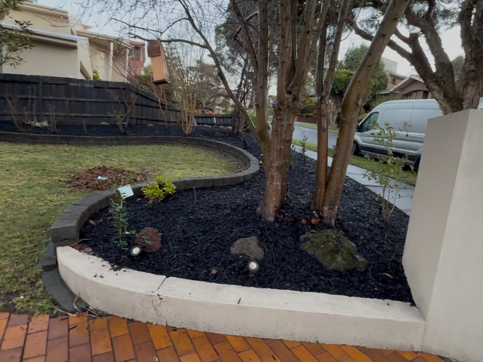 Curved garden bed with fresh black mulch and cleaned brick paving, Vermont South