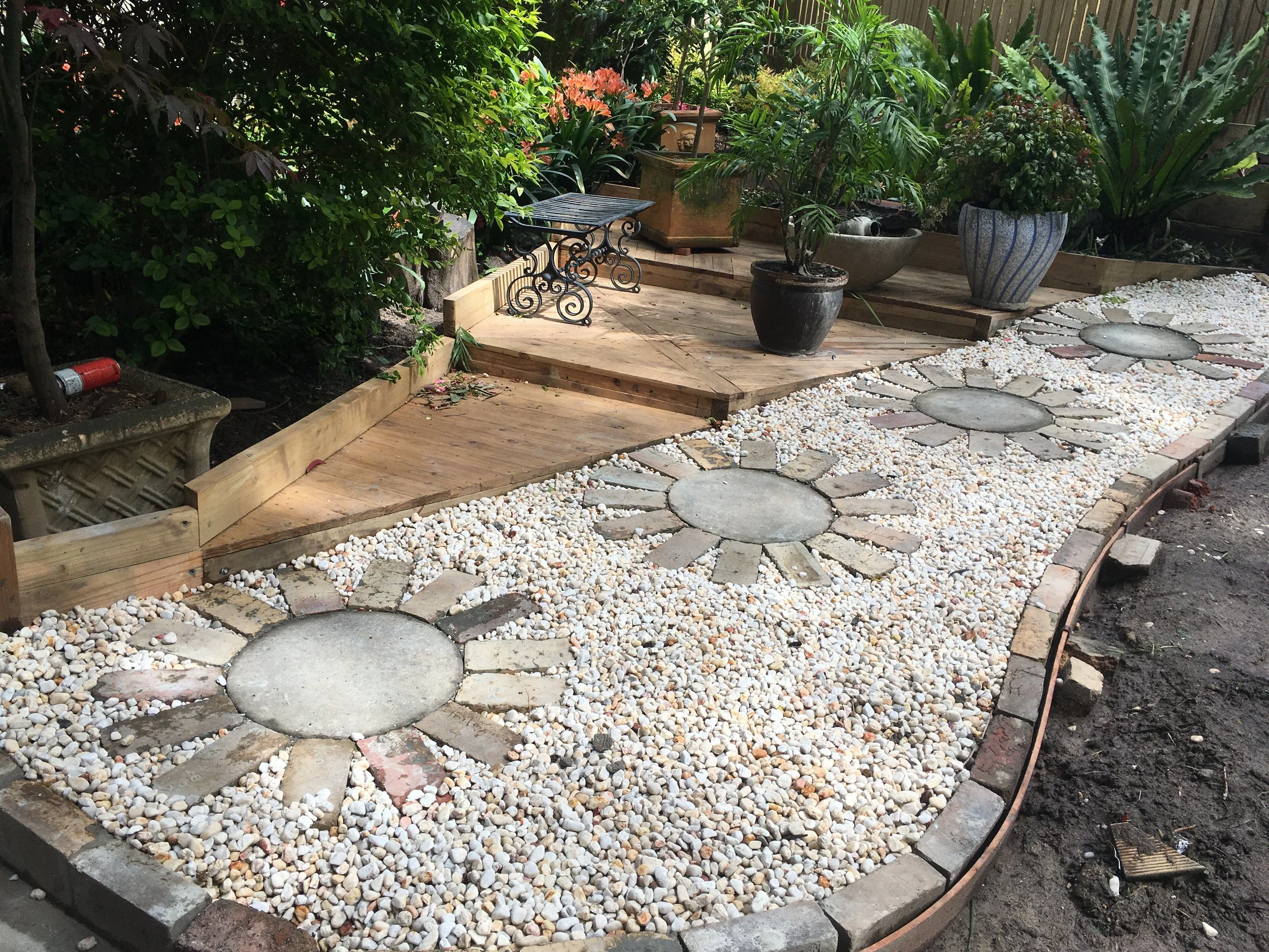 Landscaping By Mario — custom garden path and bed design featuring timber edging, white pebble borders and established container planting. Expert garden construction and design across Whitehorse, Manningham and Monash in Melbourne's eastern suburbs.
