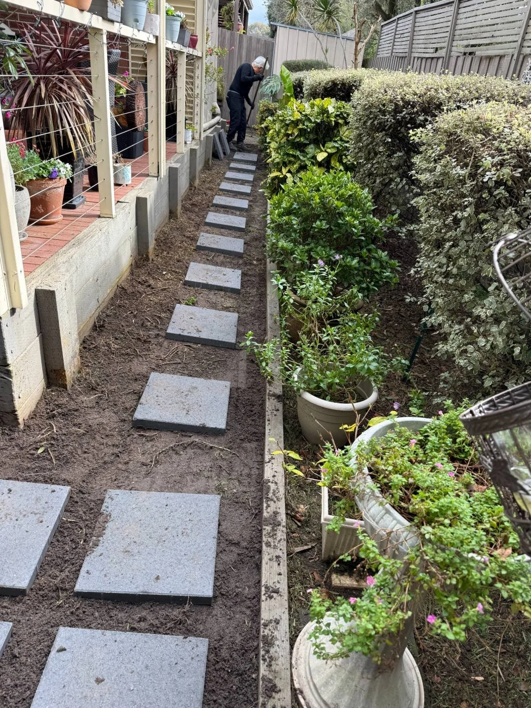 Square concrete pavers set as stepping stones along a side path before weed mat goes down