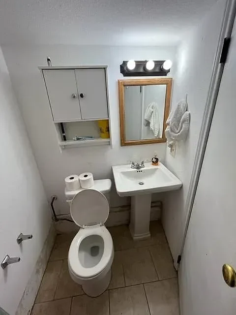 Small bathroom with a toilet, a wall-mounted cabinet, a mirror, a towel, and a small sink.