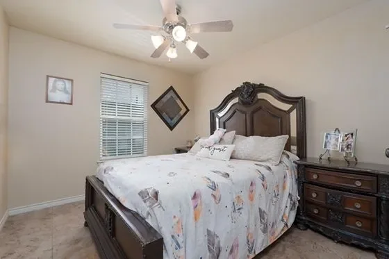 Bedroom with a dark wooden bed, white bedding, and a matching dresser. There is a ceiling fan with lights, a window with blinds, and framed pictures on the walls.