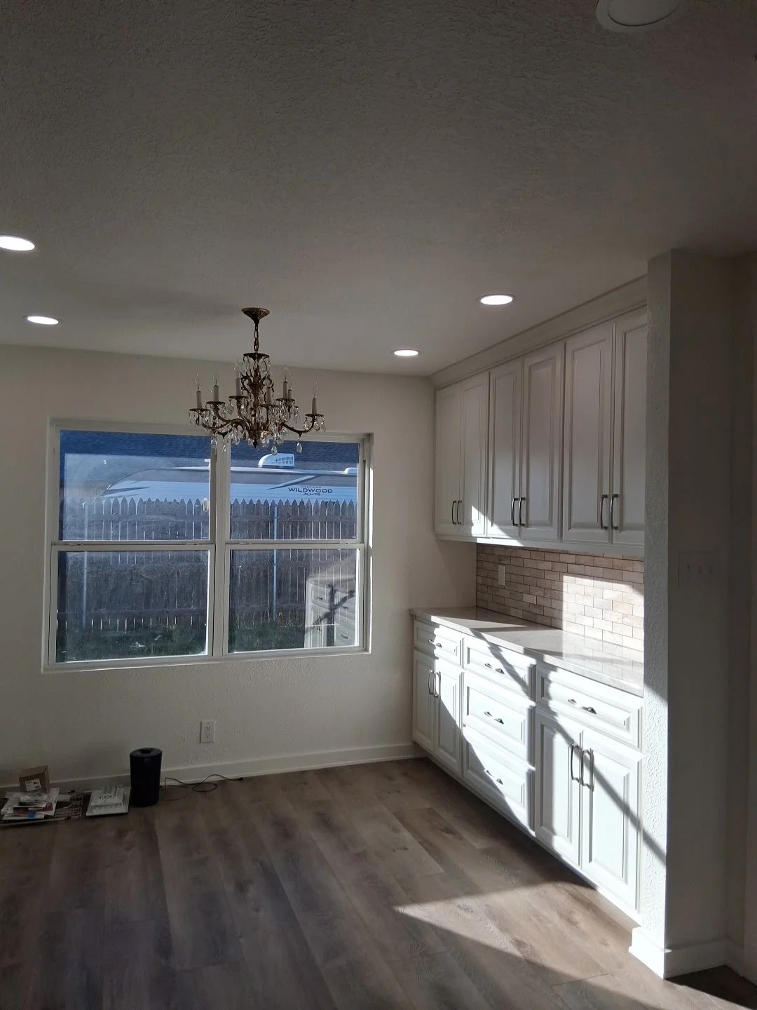 Bright kitchen with white cabinets, hardwood flooring, a window, and a chandelier, illuminated by natural sunlight.