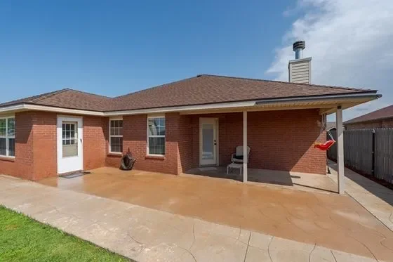 The back of a brick house with a covered patio, a chimney, a white door, and a small grassy area.