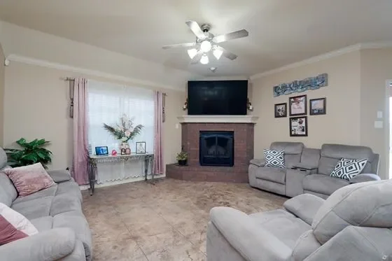 Living room with beige walls, a ceiling fan, a mounted TV above a brick fireplace, a gray sofa set, and a glass table with plants and decorations.