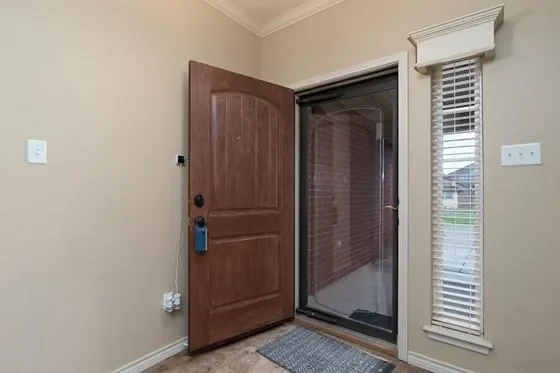 View of an apartment door opening to a screened porch or balcony, with a small rug on the floor and a window covered with blinds to the right.
