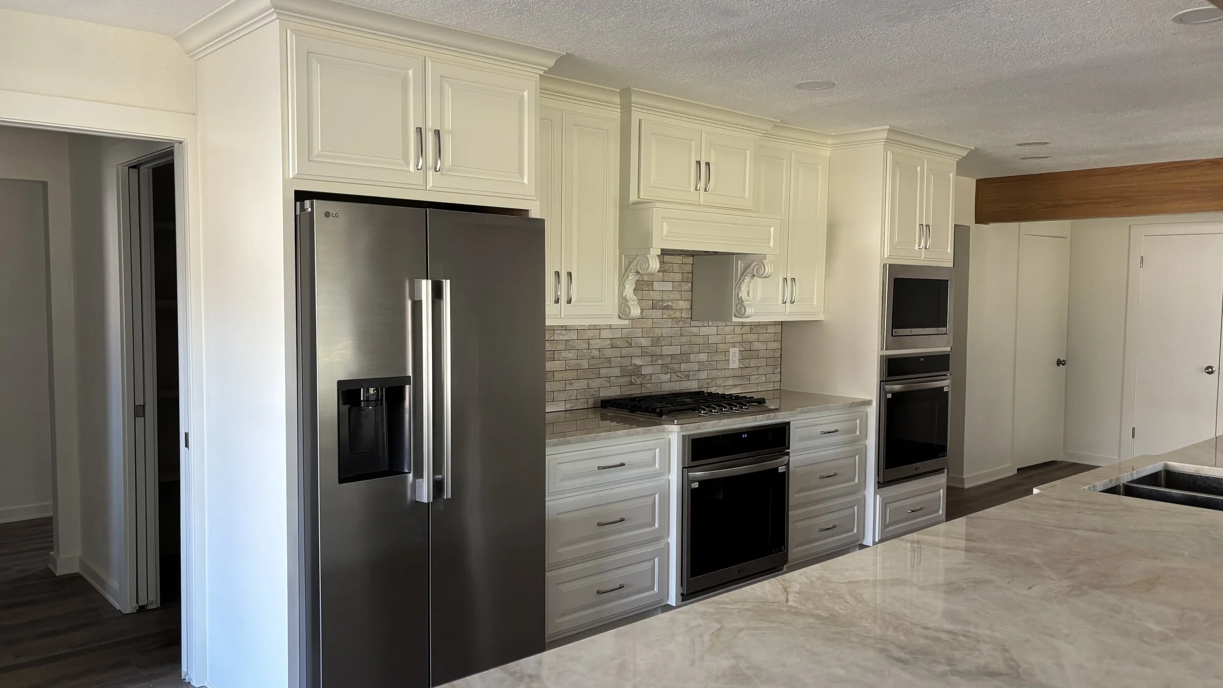 Modern kitchen with white cabinets, stainless steel refrigerator, brick backsplash, and built-in oven and microwave.