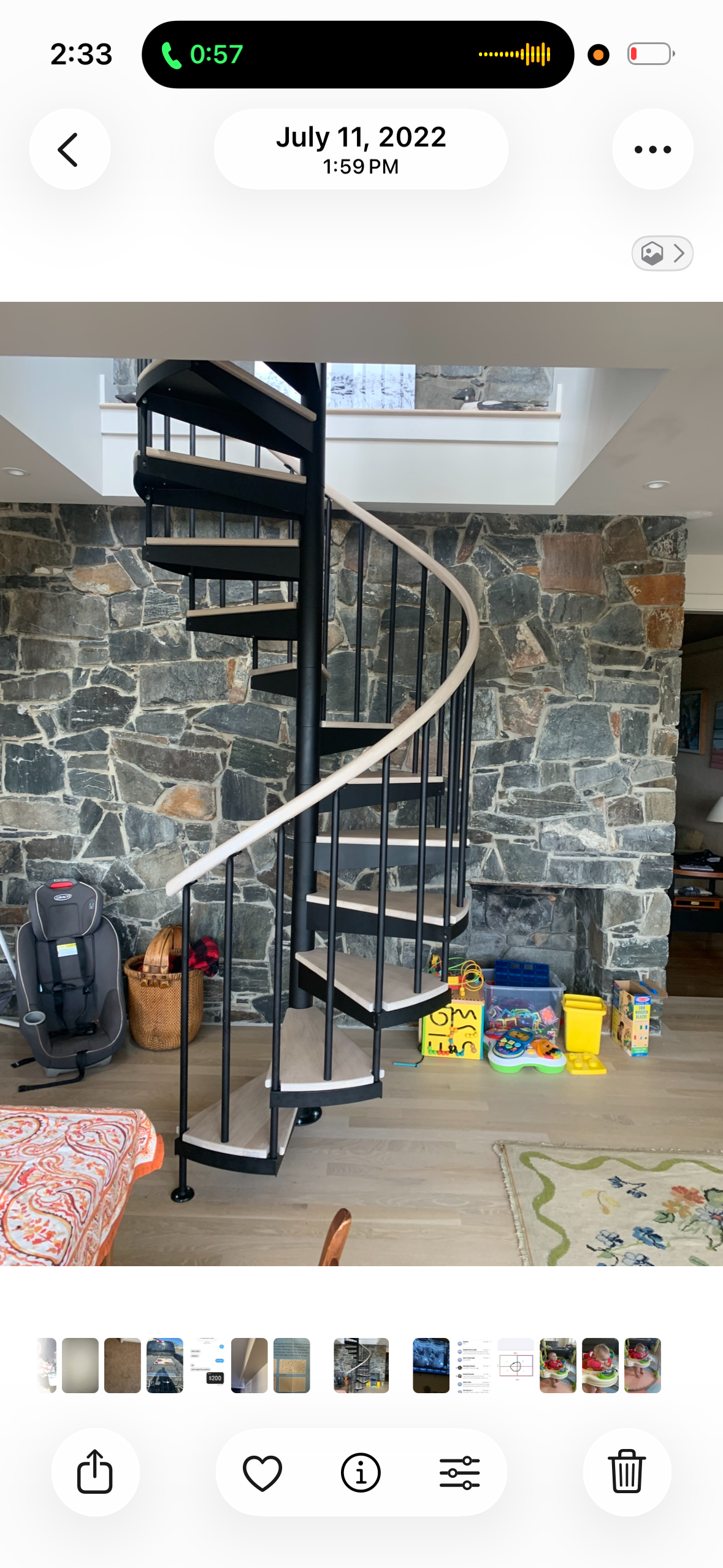 Spiral staircase next to a stone wall with children's toys and a child's car seat on the floor.