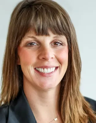 A woman with shoulder-length brown hair smiling at the camera, wearing a black top.