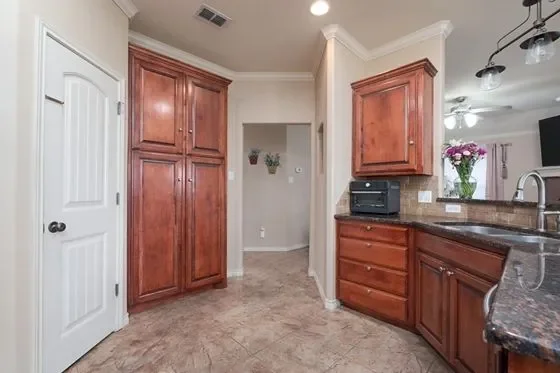 Kitchen with wooden cabinets, granite countertops, a black printer, and a vase of pink flowers on the counter.