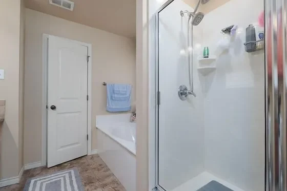A bathroom with a closed white door, a blue towel hanging on a towel rack, a bathtub, and a glass shower stall with shower essentials inside.