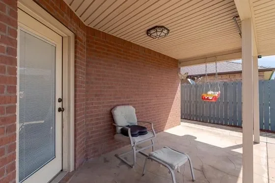 Back porch area with a metal chair, small ottoman, and a fenced backyard with a red and yellow swing.