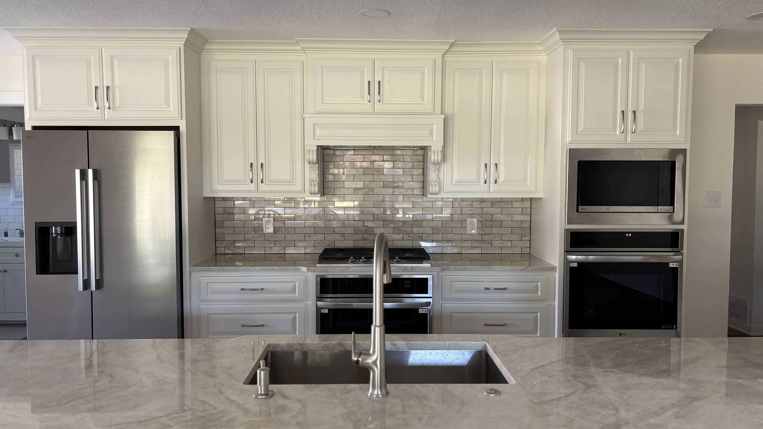 Modern kitchen with white cabinets, stainless steel refrigerator, built-in microwave and oven, brick backsplash, and a kitchen island with a sink.