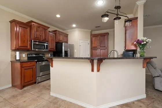 Modern kitchen with wooden cabinets, stainless steel appliances, a half-wall counter with a sink, and a vase of flowers on the counter.