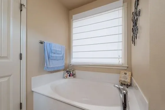 Bathroom with a bathtub, a blue towel hanging on a towel bar, a window with horizontal blinds, and decorative wall art.