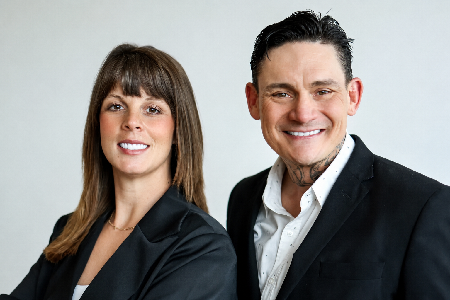 A smiling man and woman in business attire against a plain background.