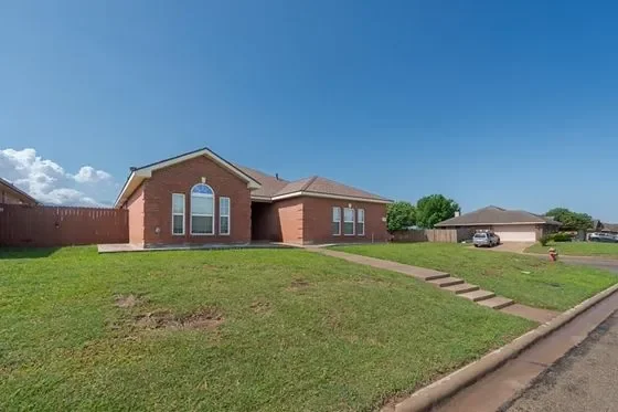 Single-story brick house with a front lawn, staircase, and a driveway with a parked car, under a blue sky.