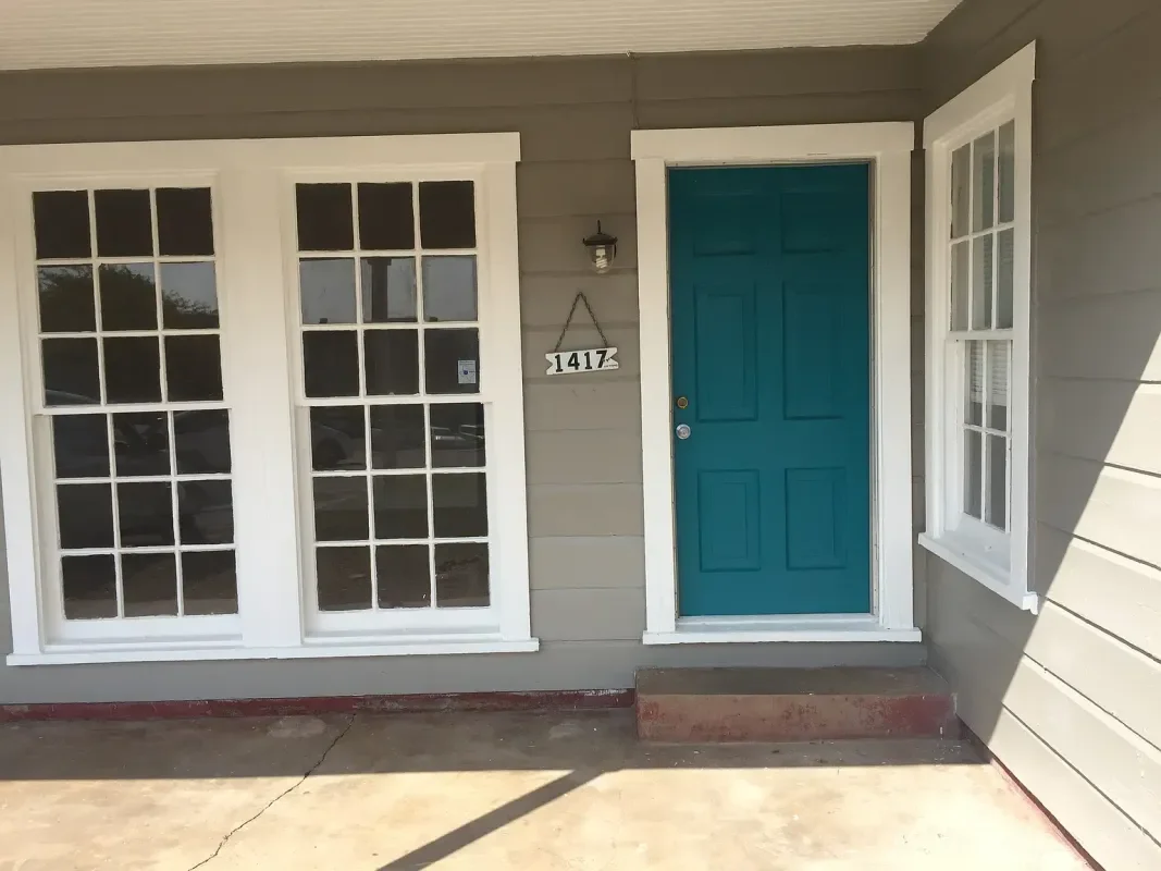 Front door house with teal door, large window panes, house number 1417, and small step, on concrete porch.