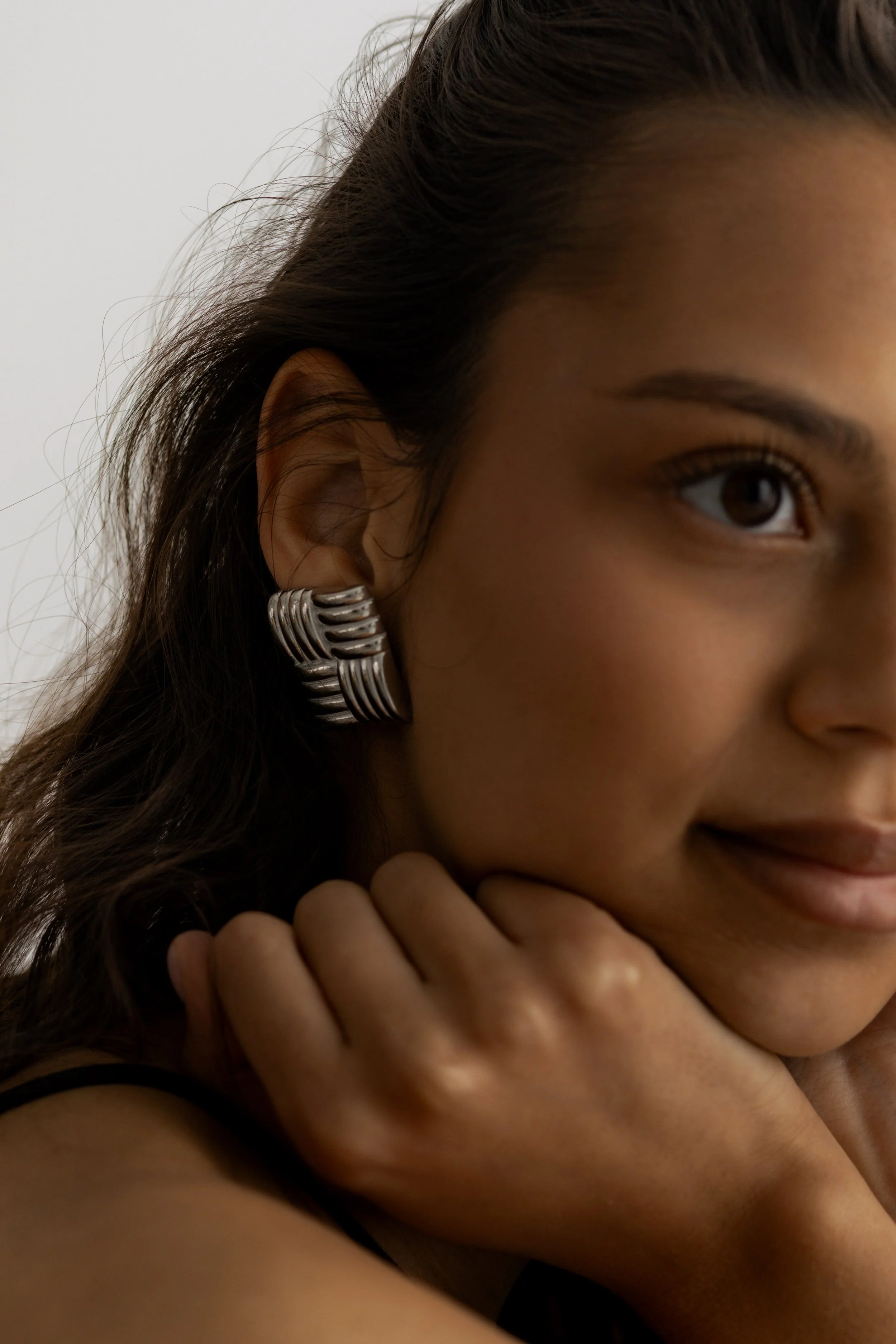 Close-up of a woman's face, showing her hair, eye, and part of her cheek with her hand resting near her chin, wearing a silver earring.