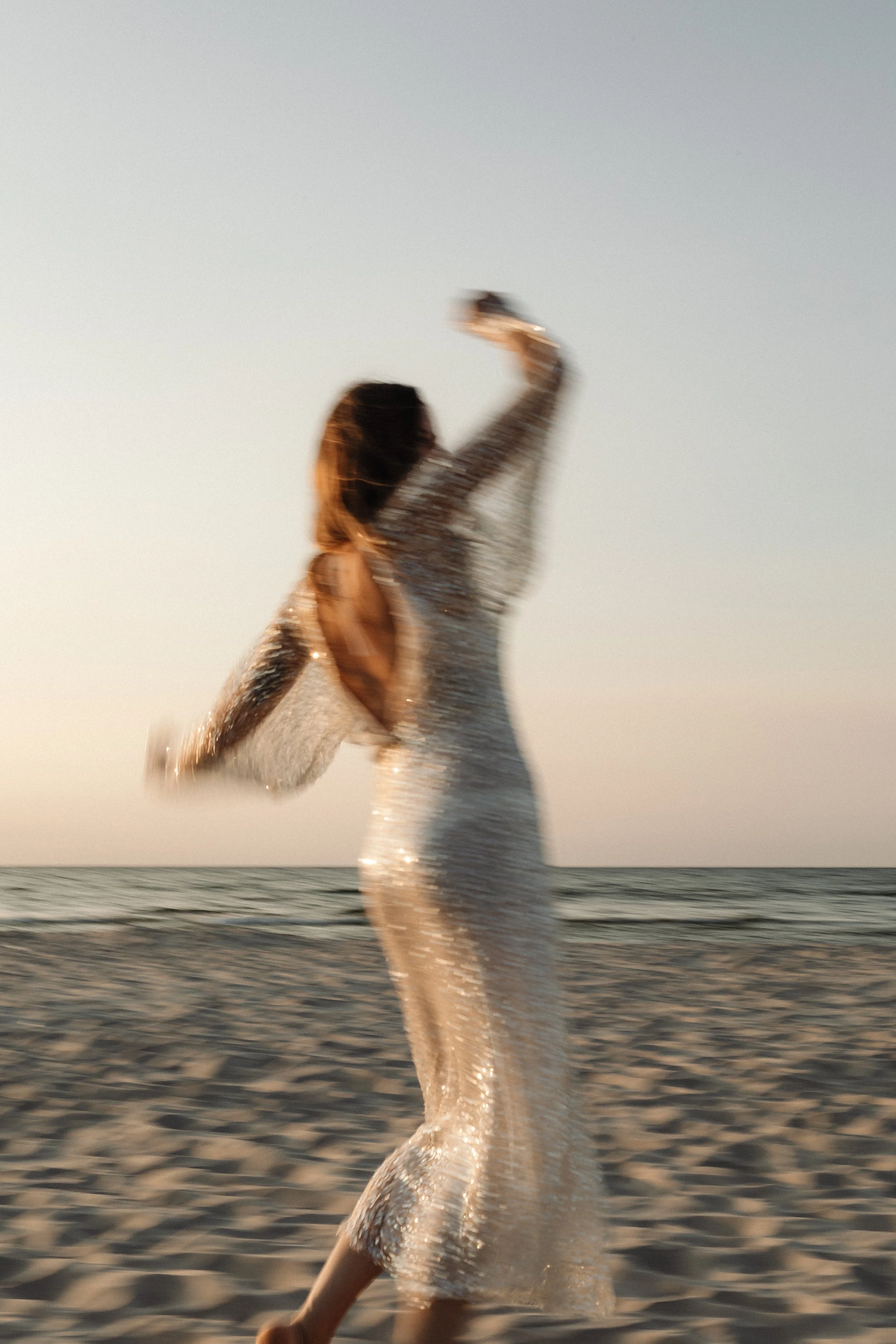 A person in a sparkly dress taking a selfie at the beach during sunset.