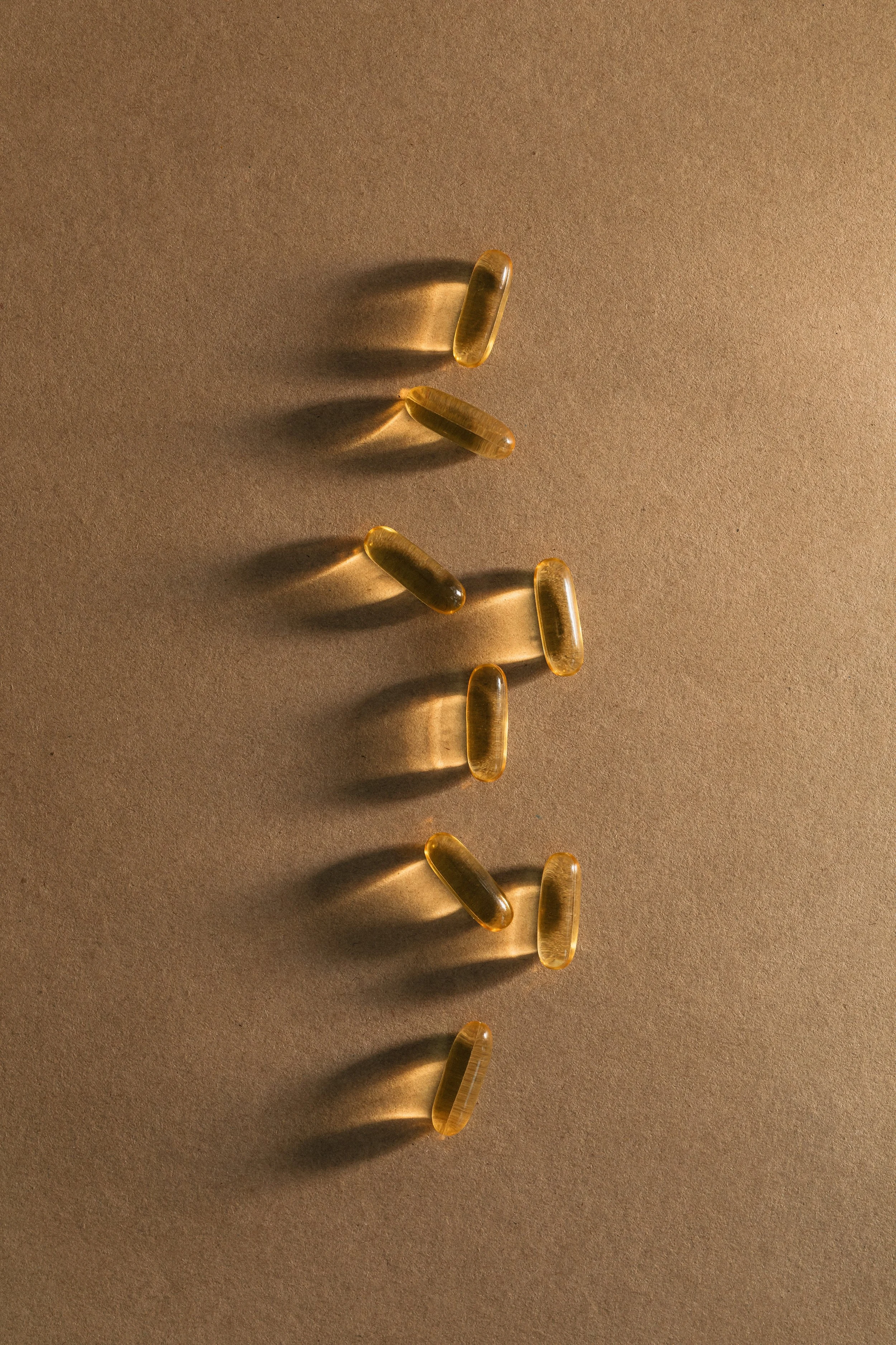 Several yellowish, translucent capsules are scattered on a beige surface, casting shadows underneath.