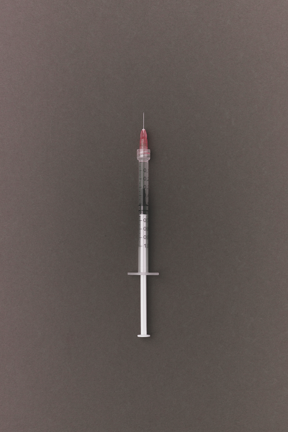 A close-up of a single-use syringe with a needle on a gray background.