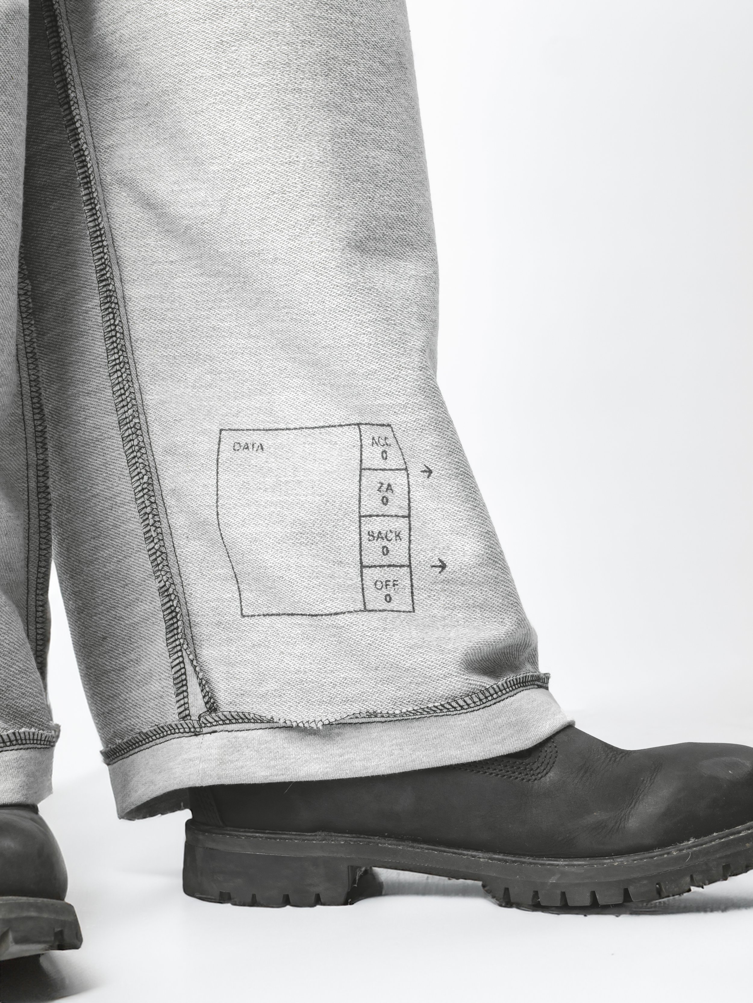 A close-up of hiking gear, showing a pair of grey hiking boots and grey cargo pants with a thermometer and data chart printed on the pants.